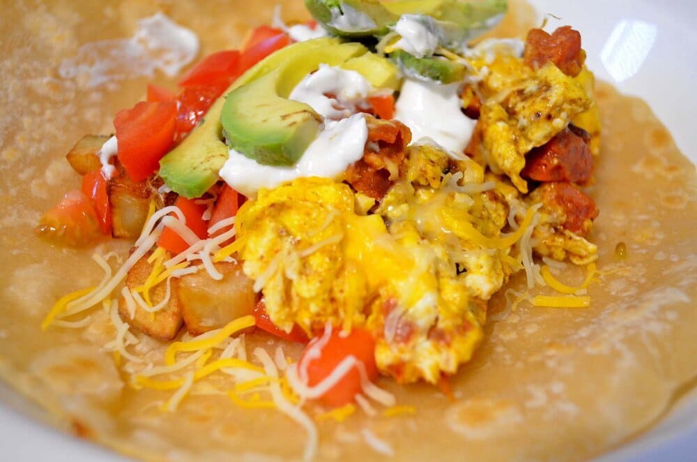 Malaysian curried chorizo eggs with fried potatoes, tomatoes, sour cream, avocado &amp; shredded cheese